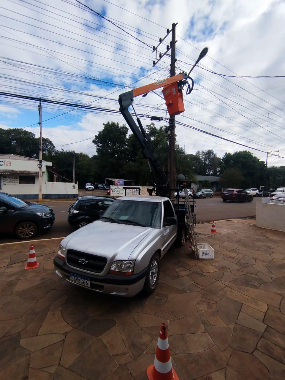 Caminhonete prata com cesto aéreo laranja trabalhando em poste de energia