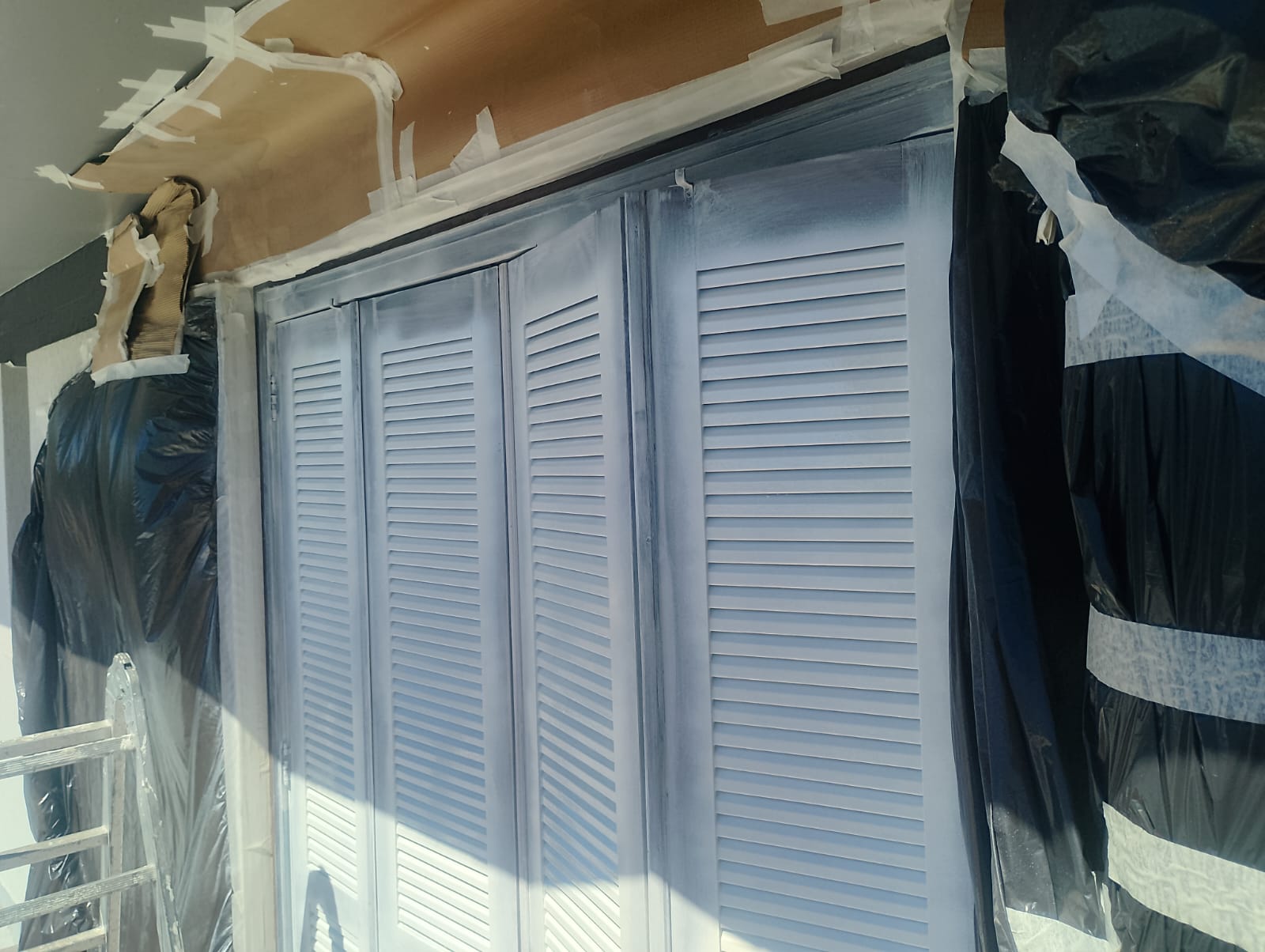 Armário embutido com portas venezianas recém-pintadas de branco, com paredes e móveis ao redor protegidos por 